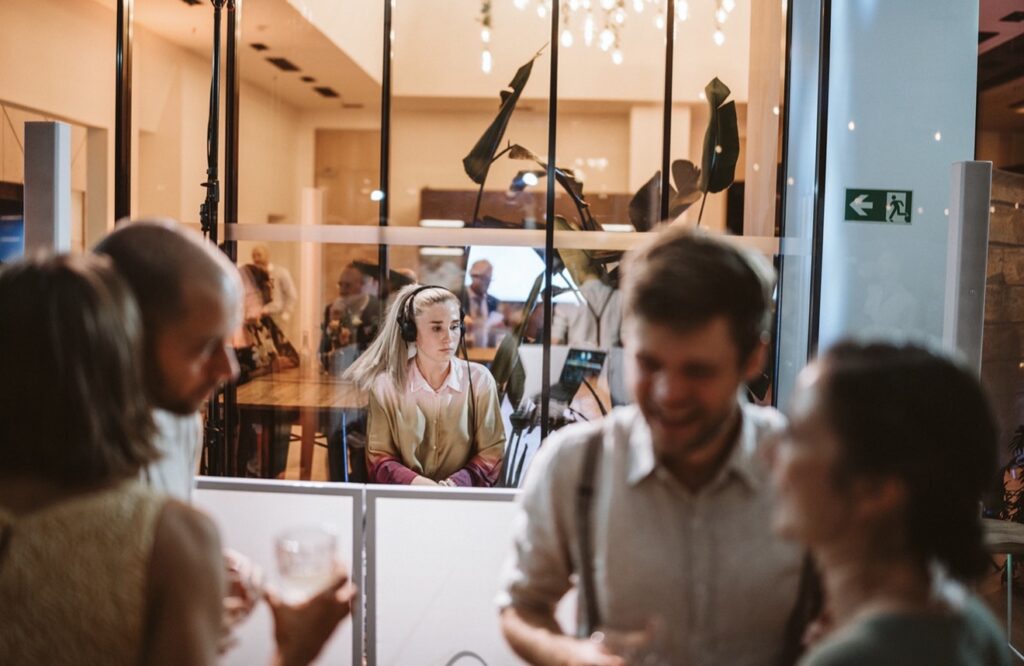 DJane Polly legt bei einem Firmenevent hinter Glas auf, Gäste im Vordergrund